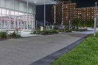 some benches and lights near the building at night's edge of park and sidewalk