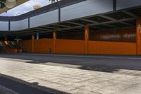 a man rides his bicycle past the orange walls of an outdoor building near stairs and benches