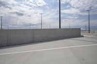 a paved parking lot with several street lights and a concrete wall against a blue sky