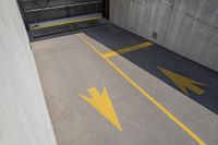 the floor of a parking garage with arrow painted in yellow and grey tones with stairs up to them