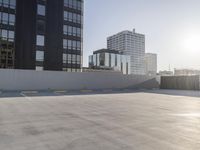 empty parking lot with city view outside of buildings, in front of a wall and sun shining