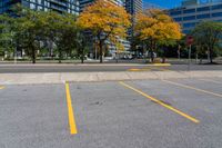 an empty parking lot in the city with tall buildings in the background and bright trees around