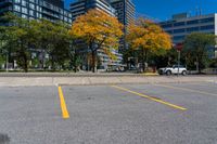 an empty parking lot in the city with tall buildings in the background and bright trees around