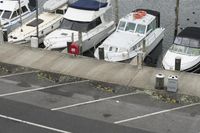 a parking lot has several parked boats in it and one boat is near by the dock