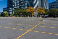 an empty parking lot in front of modern buildings with tall towers in the background and trees around