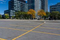 an empty parking lot in front of modern buildings with tall towers in the background and trees around