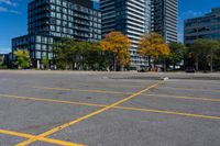 an empty parking lot in front of modern buildings with tall towers in the background and trees around