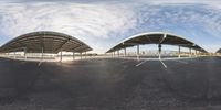 a panoramic view shows an empty parking lot surrounded by trees and buildings as seen from underneath the pavement