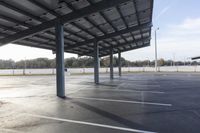 parking lot with an open space beneath a roof with poles and lights on it, next to another parking lot