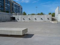 the empty parking lot in front of a wall with apartment buildings on it and a skateboarder on a ramp