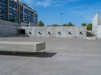 the empty parking lot in front of a wall with apartment buildings on it and a skateboarder on a ramp