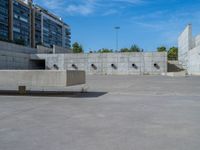 the empty parking lot in front of a wall with apartment buildings on it and a skateboarder on a ramp