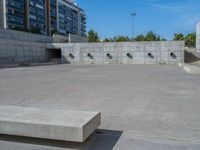 the empty parking lot in front of a wall with apartment buildings on it and a skateboarder on a ramp