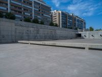 the empty parking lot in front of a wall with apartment buildings on it and a skateboarder on a ramp