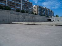 the empty parking lot in front of a wall with apartment buildings on it and a skateboarder on a ramp