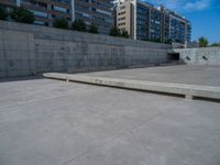 the empty parking lot in front of a wall with apartment buildings on it and a skateboarder on a ramp