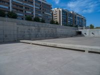 the empty parking lot in front of a wall with apartment buildings on it and a skateboarder on a ramp