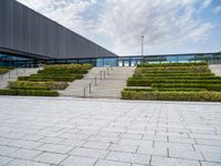 the concrete steps that lead up to a building have hedges on them and bushes on each side