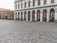 the sidewalk in front of the building is cobblestone and the clock has been set