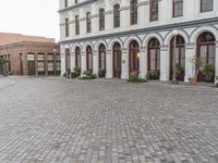 the sidewalk in front of the building is cobblestone and the clock has been set