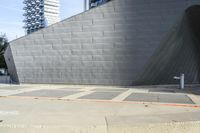 the side of an unfinished concrete building on a sidewalk with a parking meter attached to it