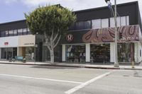 an empty street in front of store fronts and trees on the corner of the street