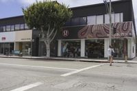 an empty street in front of store fronts and trees on the corner of the street