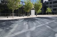 two people are walking on an empty city sidewalk by some buildings, and several trees, and benches