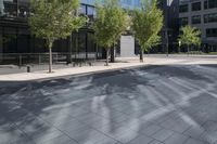 two people are walking on an empty city sidewalk by some buildings, and several trees, and benches