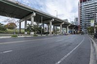 the empty roadway below an overpass in the city is gray and clean for vehicles