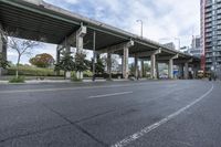 the empty roadway below an overpass in the city is gray and clean for vehicles