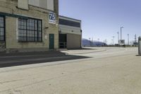 a empty street outside of a brick building with a store sign and parking lot in the background