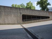 a road in the middle of a large concrete building and trees along side with a metal guardrail