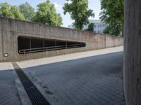 a road in the middle of a large concrete building and trees along side with a metal guardrail