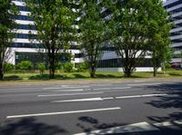 there is an empty road and green trees in the background of a building with glass windows