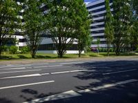 there is an empty road and green trees in the background of a building with glass windows