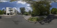 a small fisheye lens is showing the street corner of a residential area with many trees and a few cars