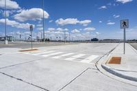 a street with a crosswalk and some buildings in the distance at the bottom with a few clouds in the sky