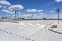 a street with a crosswalk and some buildings in the distance at the bottom with a few clouds in the sky