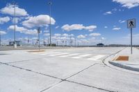 a street with a crosswalk and some buildings in the distance at the bottom with a few clouds in the sky