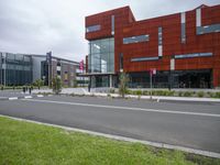 an urban road passing by a large red building with metal panels on the side of it