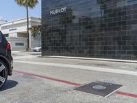 a black vehicle parked at a gas meter in the middle of the road with a building on the side and sign on the side