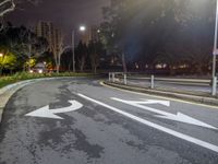 a road with three arrows that point opposite directions at night and with buildings behind it