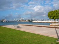 a park with a park bench and water next to it and cityscape in the background