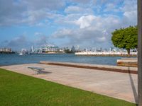 a park with a park bench and water next to it and cityscape in the background