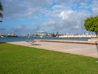 a park with a park bench and water next to it and cityscape in the background