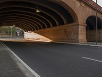 a paved road under an arched bridge with graffiti on it's sides and a sign on the side