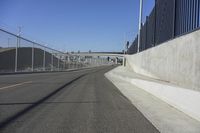 a paved roadway that runs beside a bridge with a gate on the right side and lights on either side of it