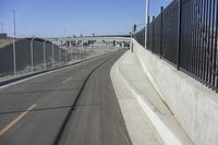 a paved roadway that runs beside a bridge with a gate on the right side and lights on either side of it