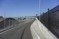 a paved roadway that runs beside a bridge with a gate on the right side and lights on either side of it